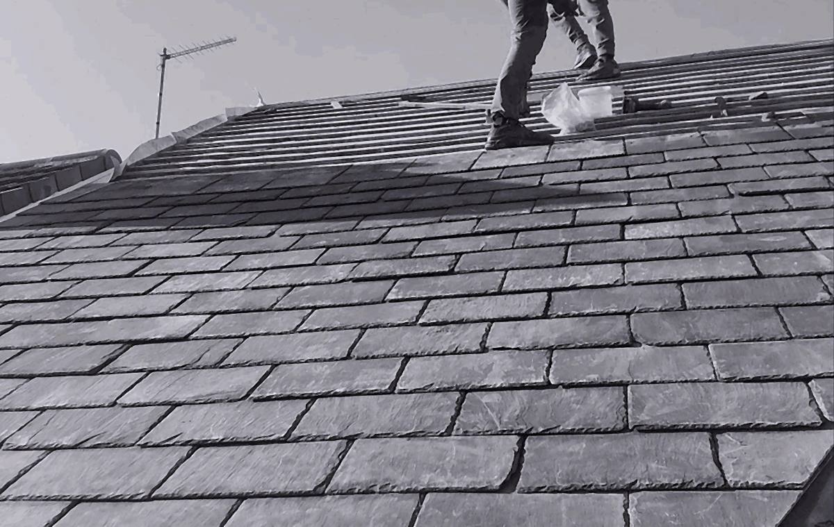 Roofer re-slating a pitched roof, with battens exposed along the ridge
